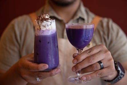 Close-up of bartender holding two bright purple drinks, one with cream