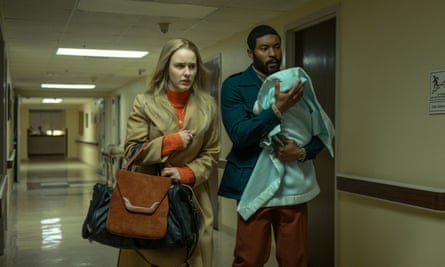 Rachel Brosnahan looking anxious with Arinzé Kene carrying a swaddled baby, walking down a hallway in a scene from I’m Your Woman.