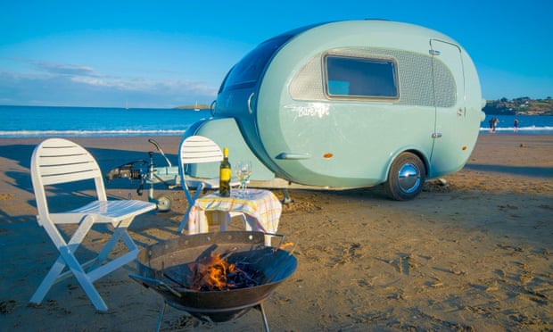 a vehicle from Barefoot Caravans parked on the beach with a table set for two