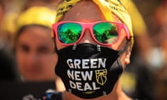 A young woman with a yellow bandana headband, pink sunglasses with green reflective lenses, and a black and white mask that reads 'Green New Deal'.