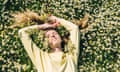 A young woman in a yellow sweater lies in a field of daisies, top view.