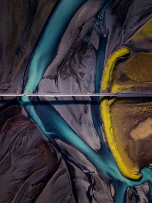An aerial shot shows a car on a bridge and the colours of the landscape