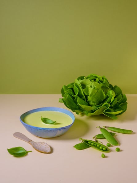 A blue bowl of pea and lettuce soup artfully arranged on a table with its ingredients and a spoon