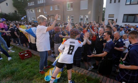 A local boy wearing a German shirt and a tartan hat given to him high-fives Scottish fans on thier fan walk to the stadium to watch Scotland v Switzerland on 19 June 2024.