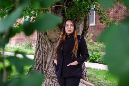 A woman with light brown hair and glasses in a black suit jacket stands in front of a tree.
