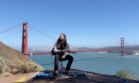 Nate Mercereau sits on a stool with his guitar synthesizer in his lap on a bluff overlooking San Francisco's Golden Gate Bridge.