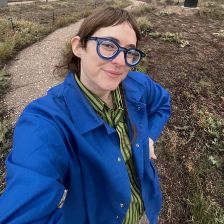 Katie, in glasses and a blue jacket, smiles for a selfie on an outdoor path