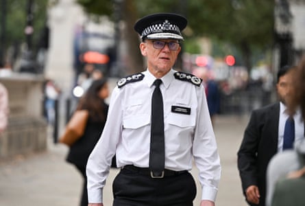 he is in a Westminster street in a uniform white shirt, black tie and hat but without a jacket; he looks as if he is walking quickly and purposefully.