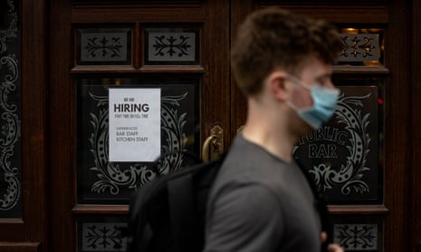 Masked man walks past recruitment sign in the window of a London pub.