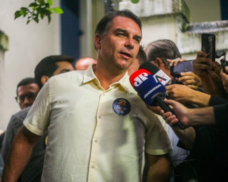 Flávio Bolsonaro speaks to people holding microphones in his direction