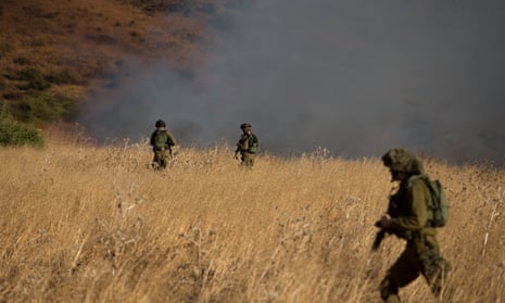 Israeli soldiers patrol next to a smoke from a fire caused by a rocket