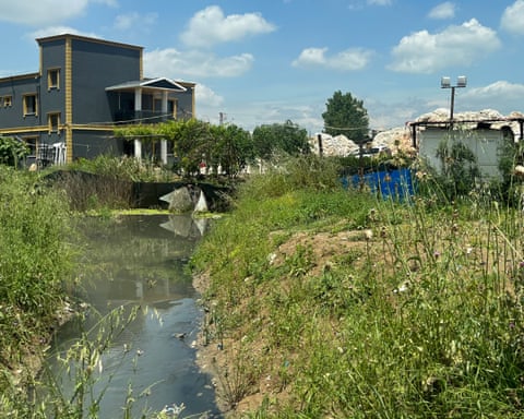 A dirty stream running between an insudtrial plant and a waste dump
