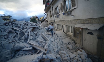 A man carries a pram among damaged buildings in Amatrice.