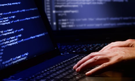 Stock photo of white hands typing on a keyboard in front of a monitor with blue code.