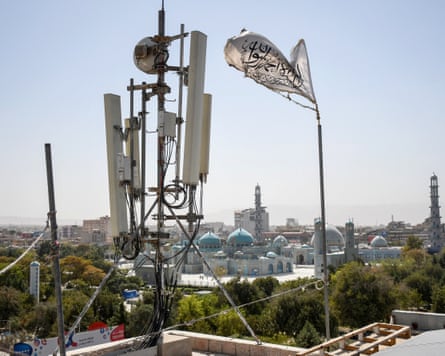 A flag with Arabic script flies next to telecom equipment with domes of a mosque in the background