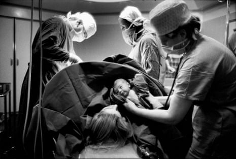 doctors gathered around woman. One doctor holds newborn
