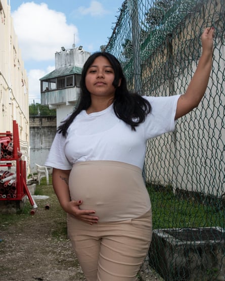 A pregnant woman holds her belly as she stands in an outdoor area of the prison