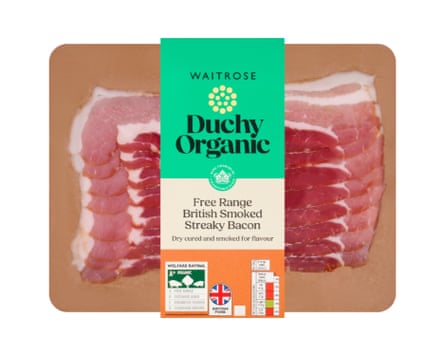 A packet of Duchy 8 Organic Smoked Dry Cured Streaky Back Bacon Rashers. There is a base wood coloured board and the rashers are clearly visible with a branded label wrapped around the middle.