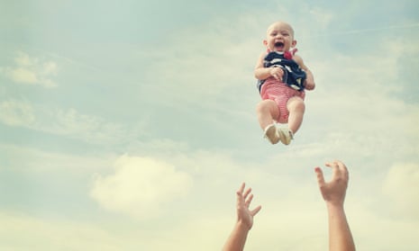Baby smiling in mid air as pair of male hands below wait to catch