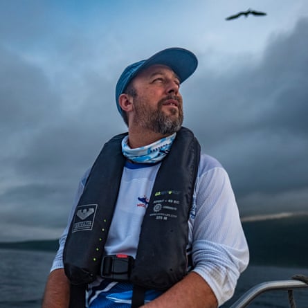 A bearded middle-aged man sits on a boat wearing a lifejacket