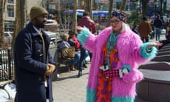 Paapa Essiedu in a beanie hat and duffle coat, Melissa McCarthy almost unrecognisable in glasses, straight blond wig, turban hat and bright pink and turquoise fluffy coat