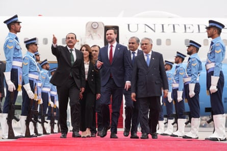 Gen Asim Munir walks alongside JD Vance on a red carpet by a plane, with ministers and officials alongside and Pakistani soldiers standing in lines on either side
