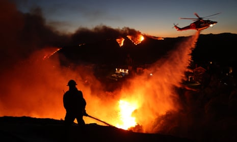 Fire personnel respond to homes destroyed while a helicopter drops water as the Palisades Fire grows