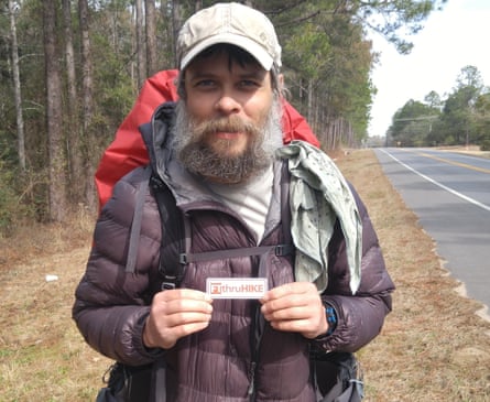 bearded man in hiking gear holding a small card