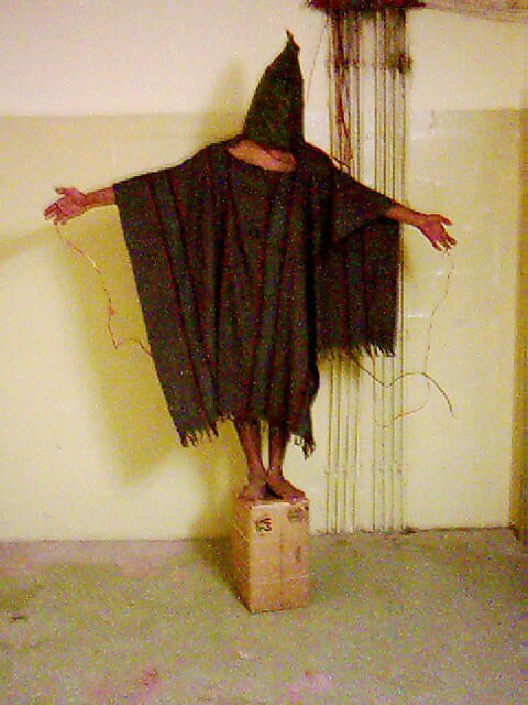 person with bag on head, arms raised and cloak over them