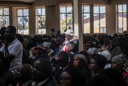 A hall packed with seated African people, with one standing woman with a hand to her face
