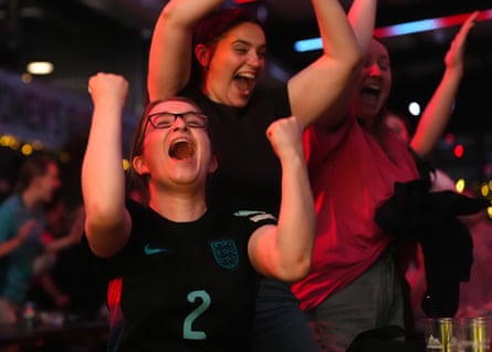 Young women jump up and cheer with their arms in the air as they watch the England v Italy penalty shootout at BoxPark Wembley
