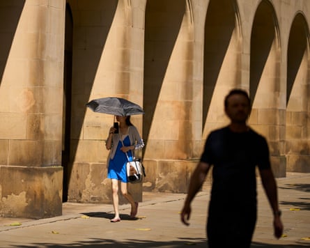 A woman uses an umbrella as shade walking next to some stone arches