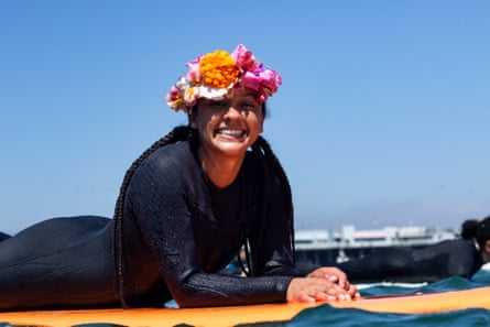 a woman wearing a flower crown smiles while lying on her surfboard