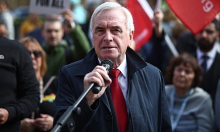 John McDonnell, in a tie and overcoat, holds his hand on a long-stemmed microphone