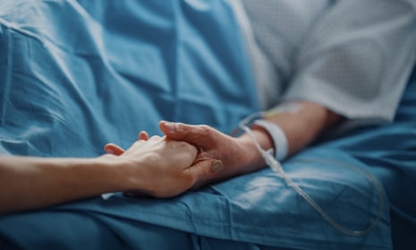 Woman holding hands with relative on hospital bed