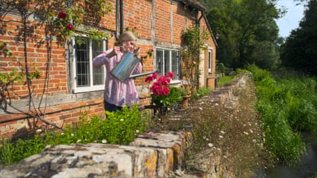 Woman watering a geranium on a wall with various plants growing all around