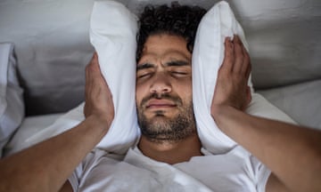 Young man in bed covering his ears with a pillow