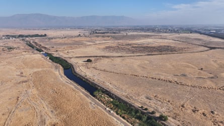 A long, narrow channel of water runs through a vast plain of parched, brown land.