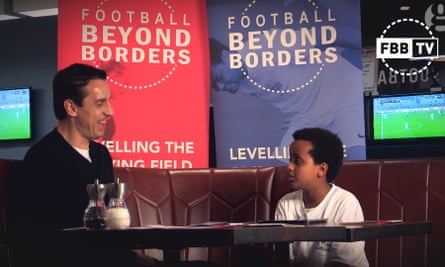 Gary Neville and a young footballer talk in front of Football Beyond Borders posters