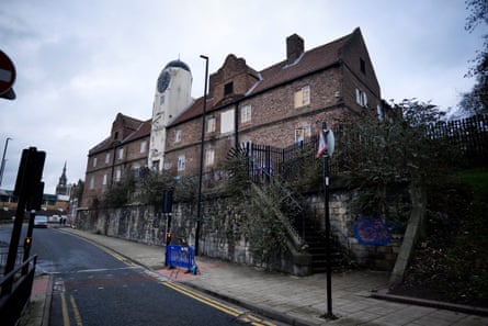 The building seen from the road; it is tall with a central white clock tower and tiled roof.
