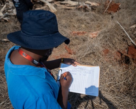 A person wearing a blue sunhat, which obscures their face, writes notes on a chart