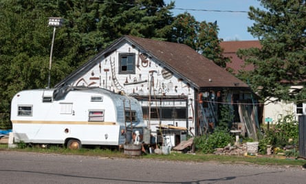 A camper trailer parked in front of a garage covered with antique farm and forestry implements