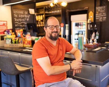 A smiling man seated at the bar in a traditional English pub