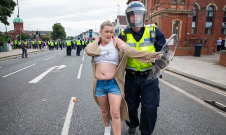 A woman is led away by police after pushing a burning wheelie bin into the police lines during the far right riots in Middlesbrough on Sunday