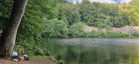 A hiker’s boots and pack sit under a tree next to a lake in the forest.