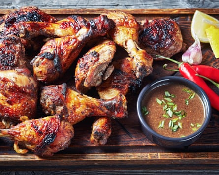 Jamaican jerk chicken presented on a dark wooden board, with chillis, lemons and salsa dip