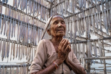 A woman prays surrounded by small fish hanging on a bamboo rack