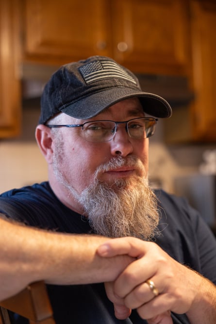A bearded man with a black ball cap with the US flag.