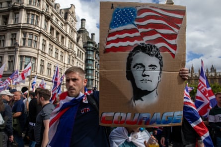 A person with a Union Jack flag around his neck carries a sign that features Charlie Kirk and the word ‘courage’