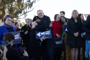 The prime minister, Anthony Albanese, hugs a participant at a rally against domestic violence in Canberra. They are surrounded by other people from the rally, including some Labor ministers, and the woman is holding a sign saying 'We won't wait. End domestic violence'